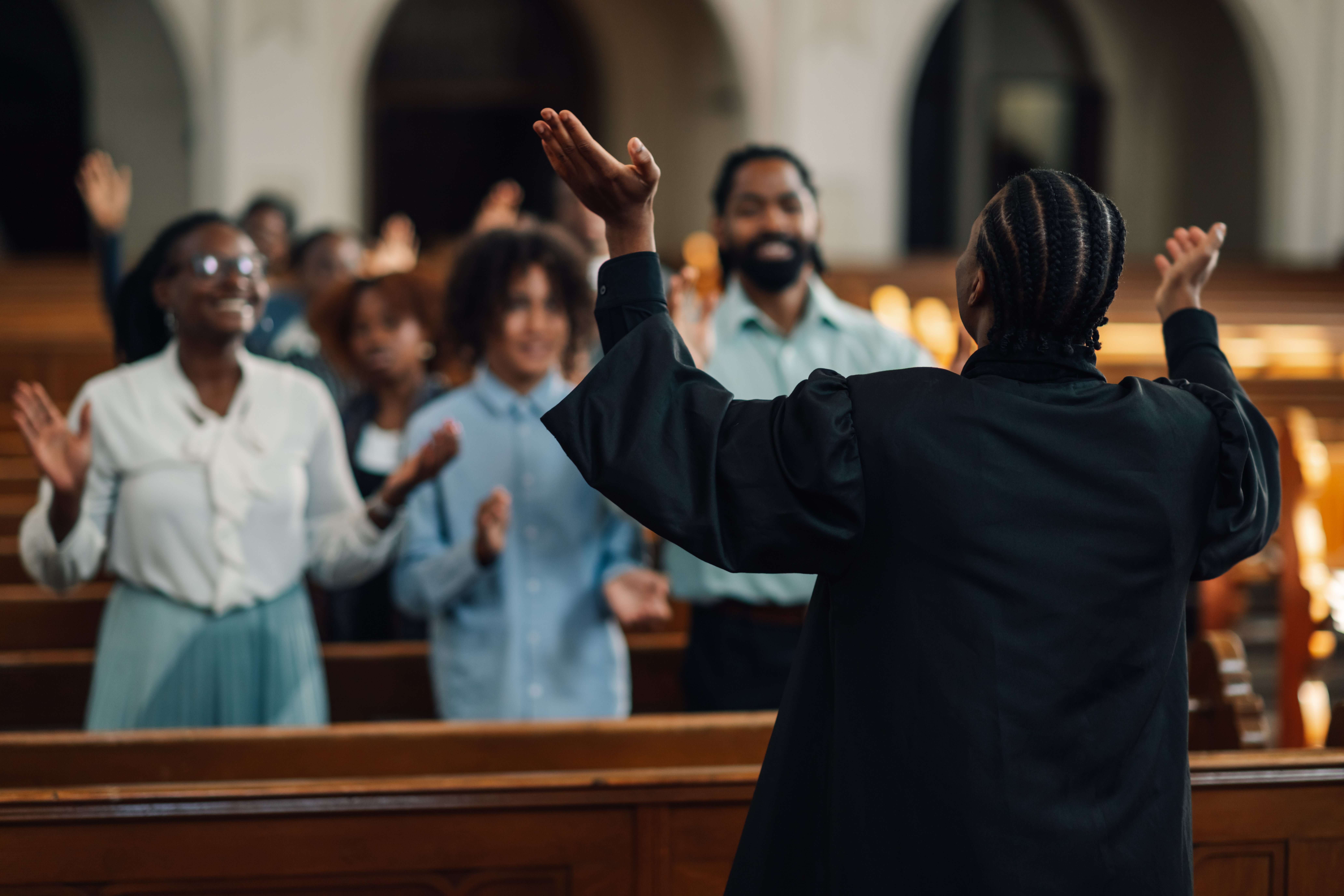 Preacher is leading a diverse congregation in prayer inside a church, with everyone raising their hands in worship. The focus is on the power of faith and the importance of community